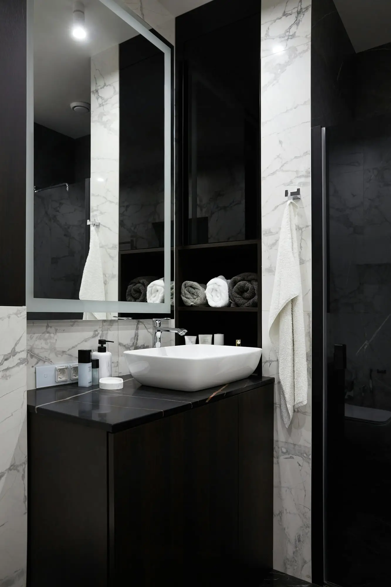 Black vanity with a white vessel sink set against white marble walls and tall black cabinetry