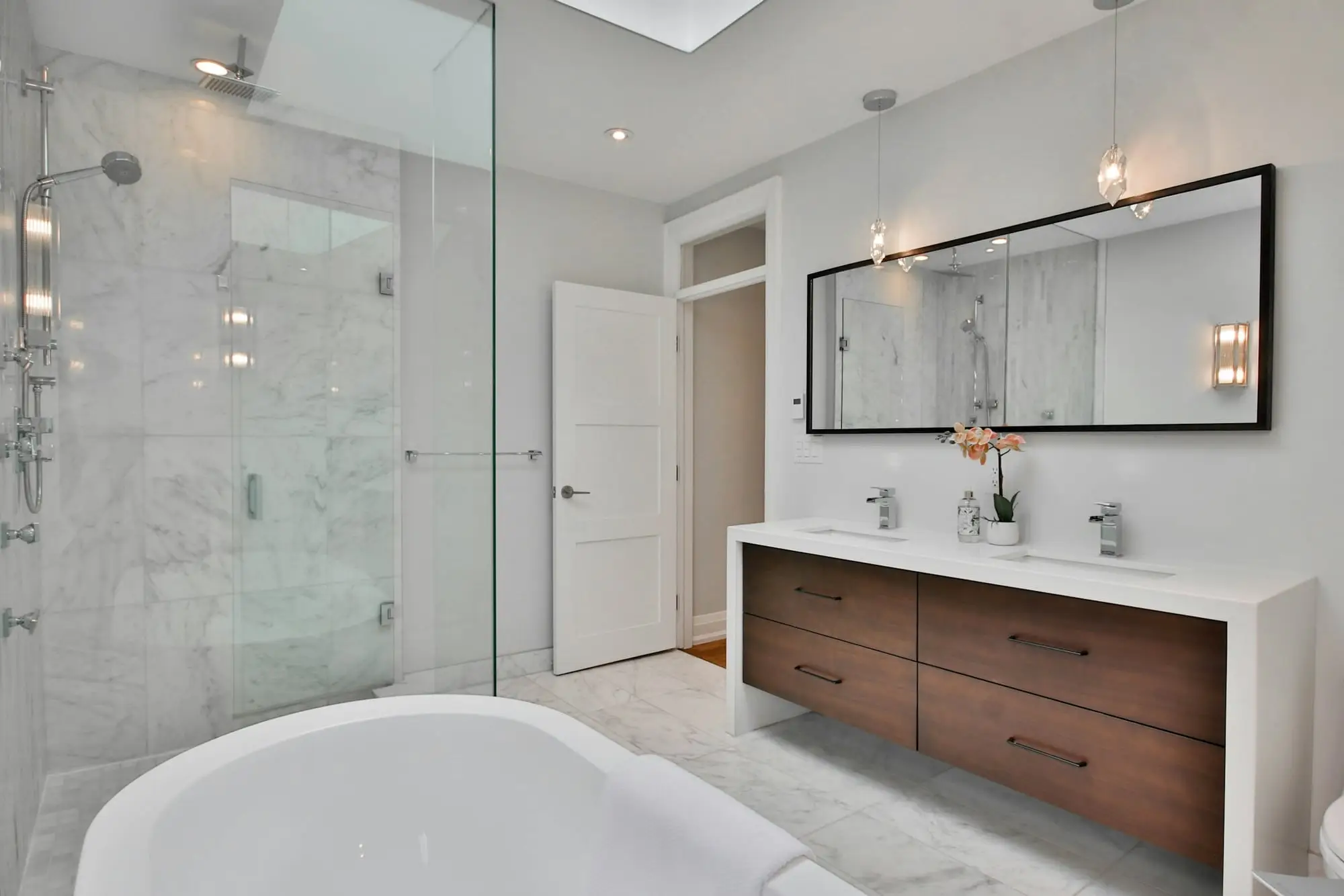 White marble bathroom with a soaker tub, glass shower enclosure and a walnut floating double vanity