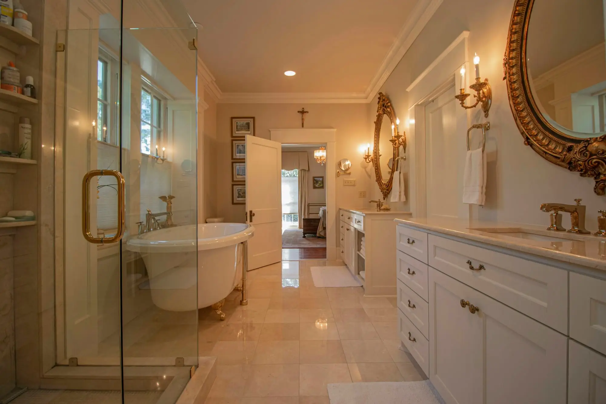 Traditional ensuite with a glass shower, clawfoot tub, white cabinetry and a gilded round mirror