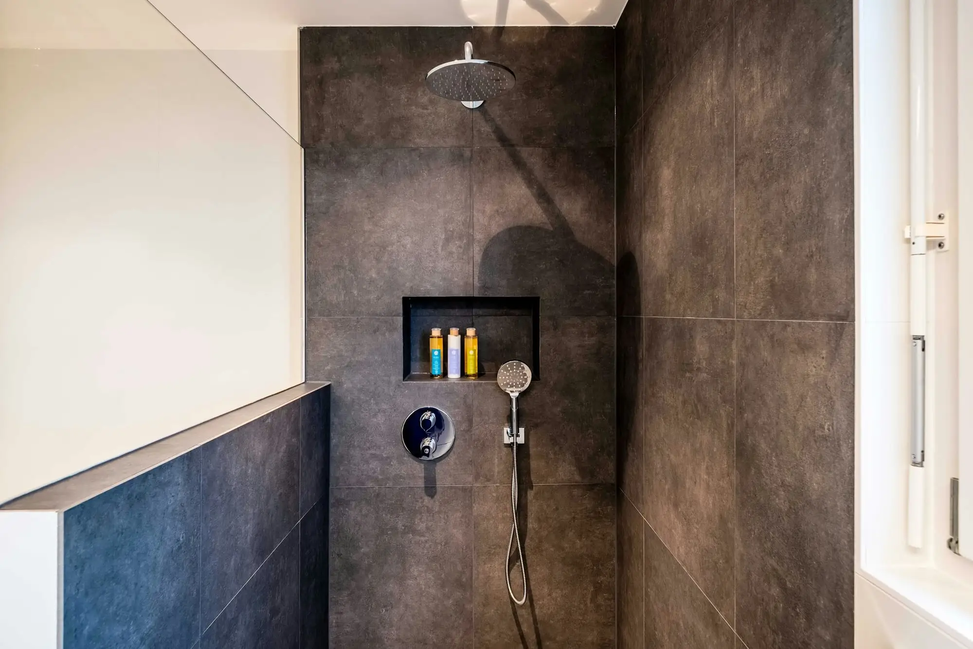 Curbless walk-in shower with large-format dark porcelain tile, a rainfall shower head and a lit wall niche
