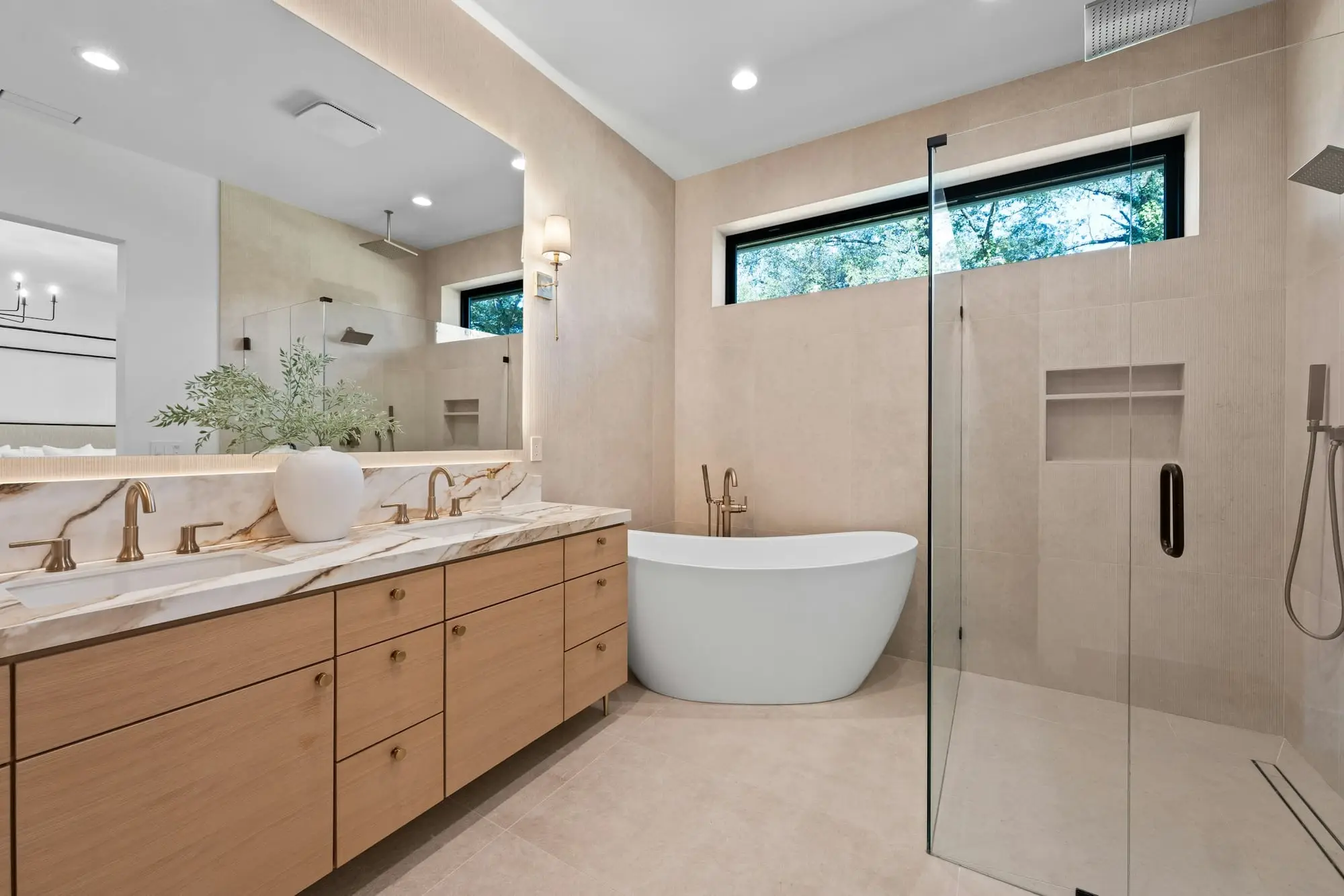 Bright primary bathroom with a freestanding tub, oak double vanity, marble counters and a glass-enclosed shower
