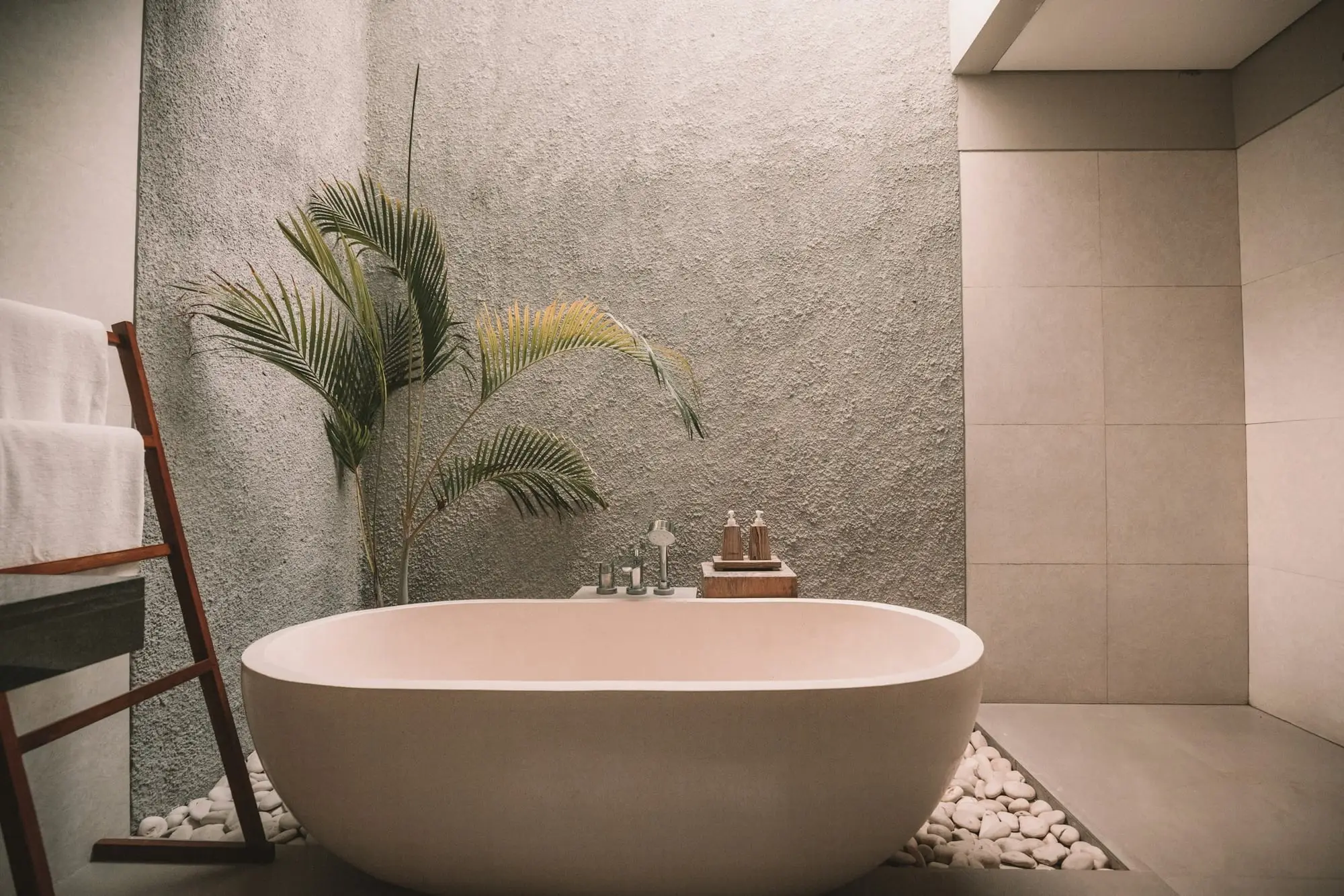 Freestanding stone-look bathtub in a calm grey bathroom with a textured plaster wall and plants