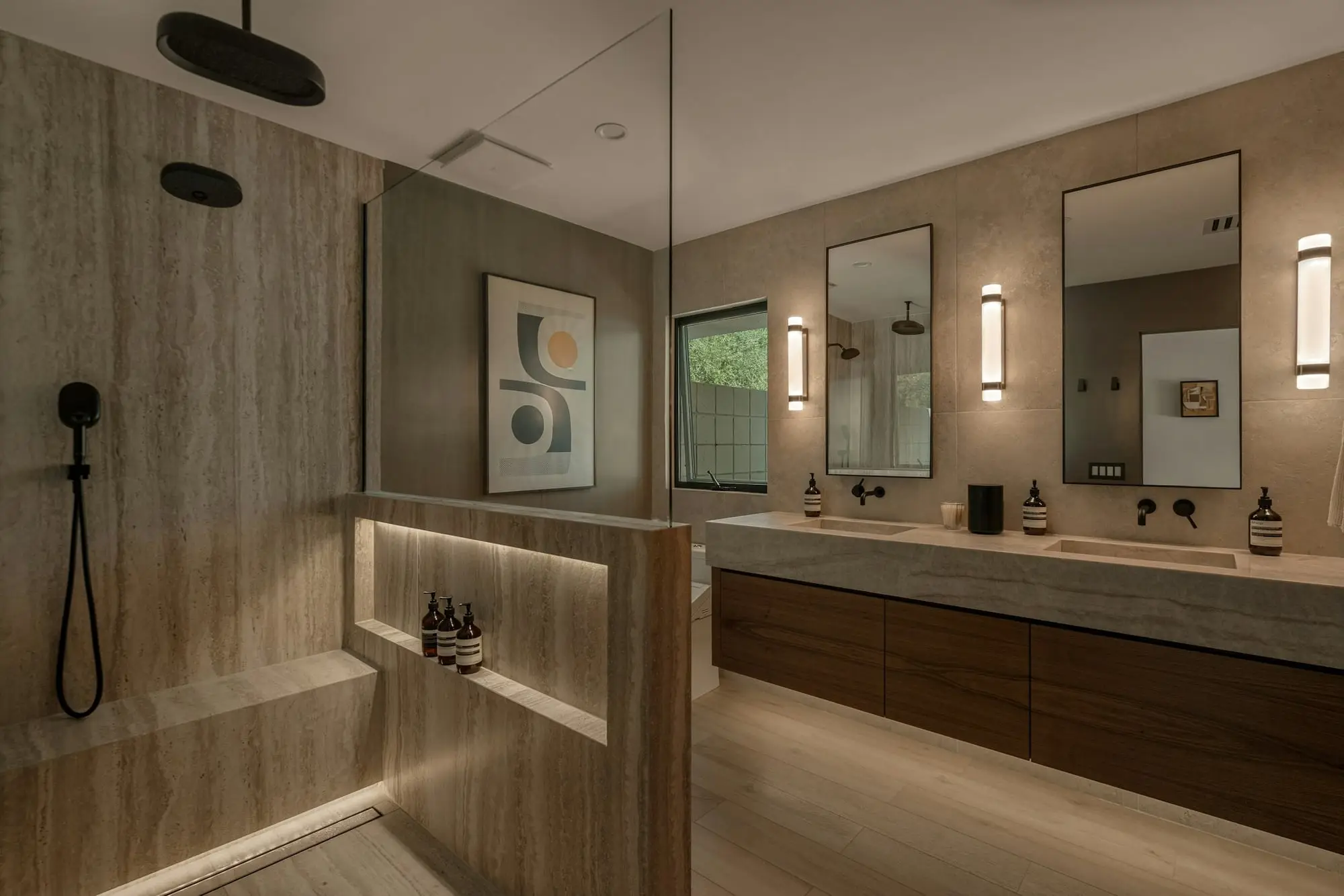 Warm-toned bathroom with a long floating double vanity, backlit mirrors and a glass walk-in shower with a built-in bench
