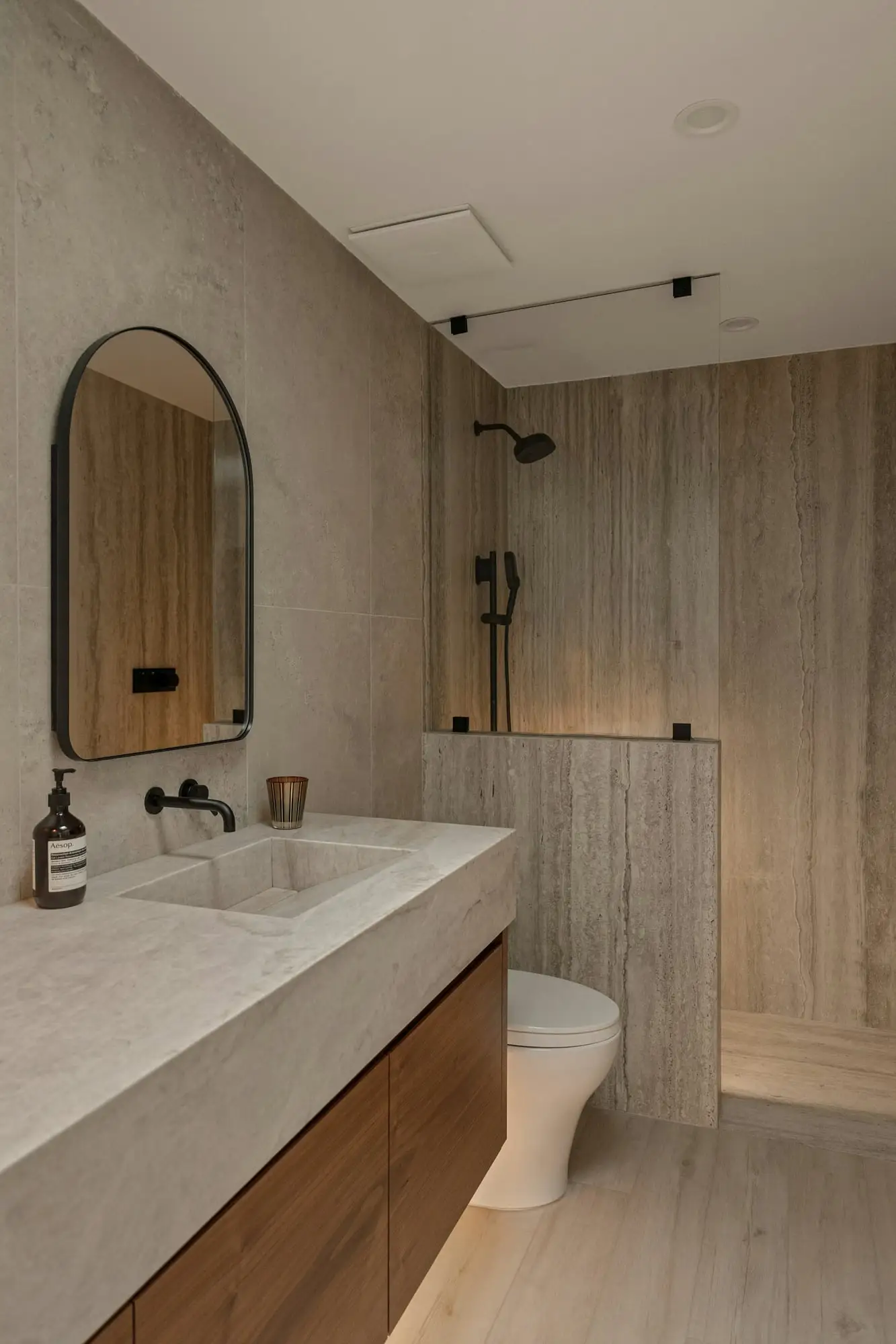 Floating wood vanity with a thick stone countertop, integrated sink, arched mirror and matte black fixtures